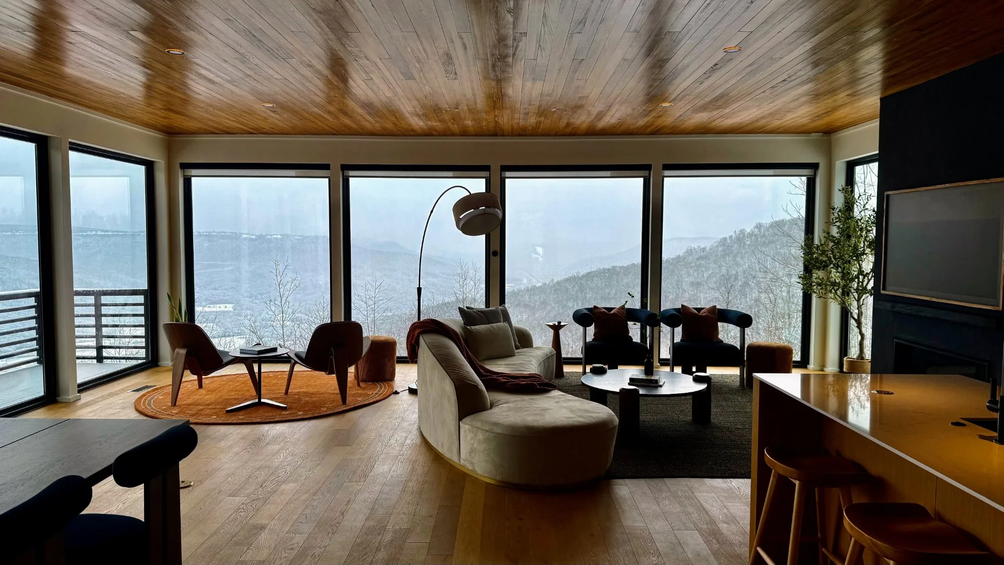 Midcentury-influenced living room with curved sofa, wood-plank ceilings, and panoramic windows facing the valley at Jackson Point
